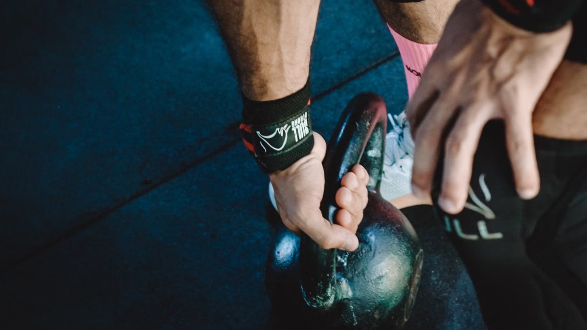 Muscular athlete lifting kettlebell during workout session, showcasing strength and fitness.